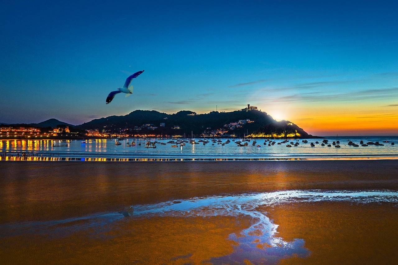 Bahía de La Concha de Donostia al atardecer, con los barcos fondeados y el monte Igueldo iluminado al fondo
