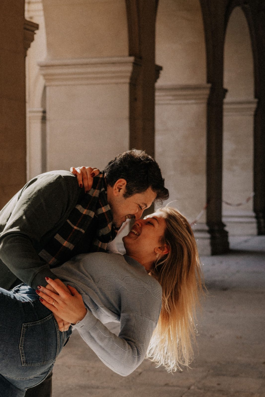 Pareja joven abrazada y riendo bajo los arcos de un claustro de piedra