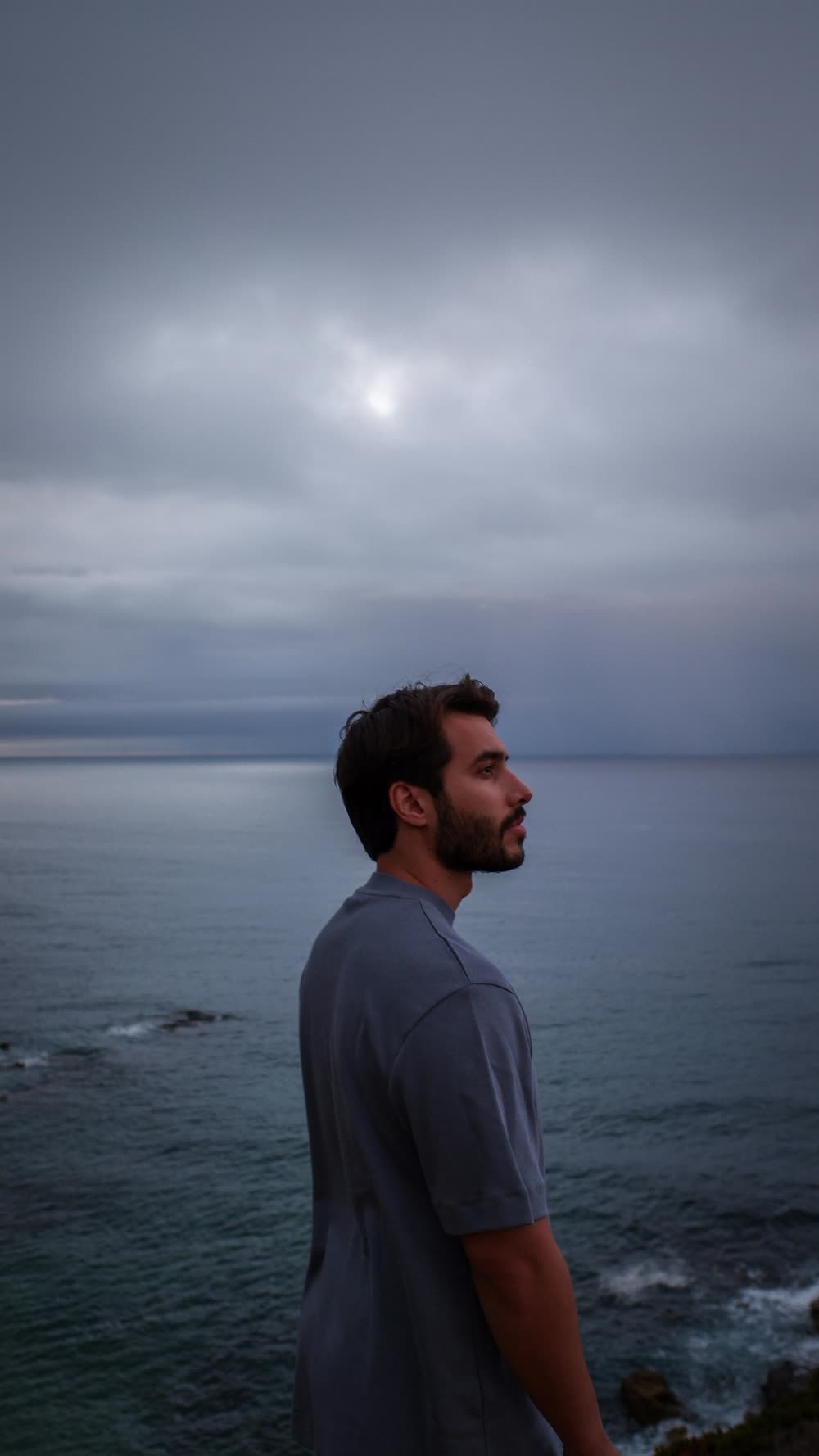 Hombre de perfil en un mirador junto al mar, mirando al horizonte bajo un cielo nublado